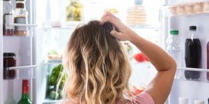 Woman scratching head in front of the fridge